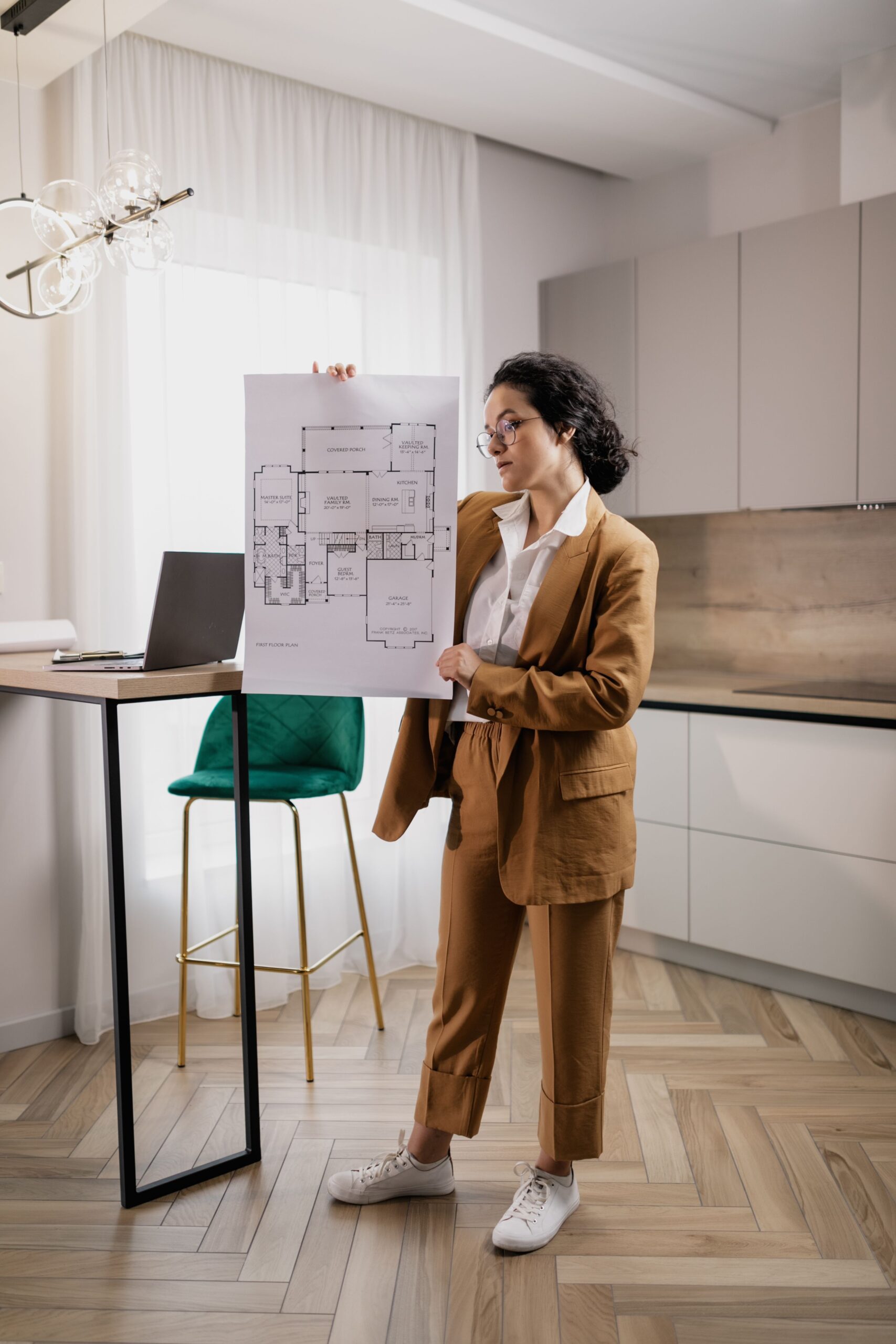 Realtor in stylish office attire presenting a detailed floor plan inside a modern kitchen setting.